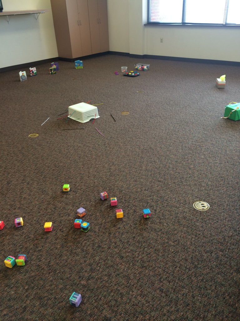 room set up for baby explorers: blocks, basket with pipe cleaners, pompoms in muffin tin with plastic tongs, ribbon tug box, board books, scarves in kleenex box